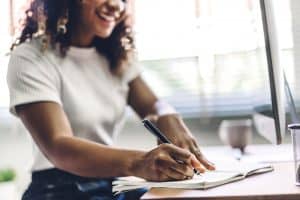 A woman smiling while writing on a notepad. Multicultural counseling in North Carolina is a great BIPOC mental health resource. Have you been looking for a 