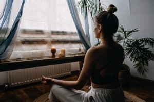 Image of a woman practicing mindfulness mediation in front of a window. Meditation is a great technique for stress management in North Carolina. We can also help with anxiety treatment in Charlotte and Asheville, North Carolina. Call today to talk with an online anxiety therapist.