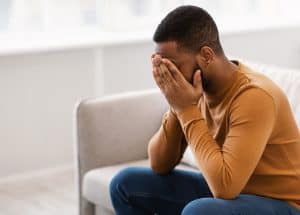 Image of an African American man in an orange shirt covering his face with his hands. You can start online therapy from Asheville or anywhere else in North Carolina. We can help you with anxiety treatment & stress management. We will help you get connected with the right online therapist in North Carolina.