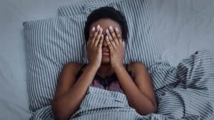 Image of a woman laying in bed with striped sheets. Do you think you are experiencing trauma symptoms or PTSD symptoms in Charlotte, North Carolina? Working with a trauma therapist in North Carolina can help! Reach out today to start trauma therapy in North Carolina. Call now!