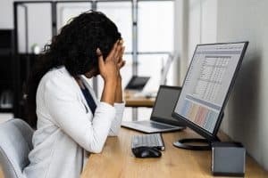 Image of a woman at her computer with her hands on her head. An online therapist in North Carolina can help you deal with stress symptoms