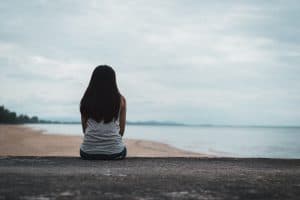 Image of a woman sitting out at the beach. Hypervigilance is just one of the many PTSD symptoms. A trauma therapist can help you identify other trauma symptoms. If you need help PTSD treatment can help you feel better. Read on to learn more.