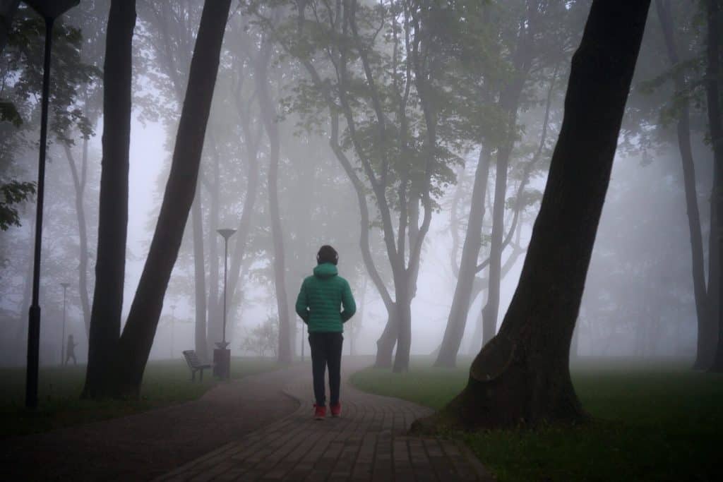 Image of a man in a green jacket suffering from fear walking through a park. A trauma therapist in North Carolina