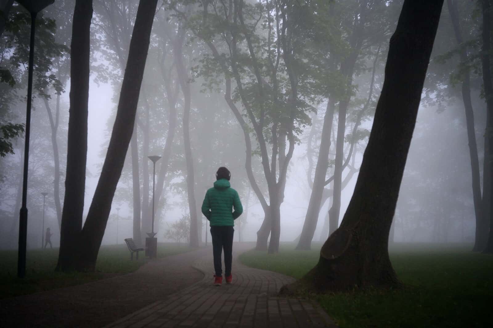 Image of a man in a green jacket suffering from fear walking through a park. A trauma therapist in North Carolina