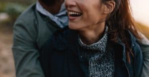 Image of a woman smiling while being hugged from behind by her male partner to show that closeness you can achieve after starting couples therapy and marriage counseling in North Carolina. Get that Jim and Pam type of relationship with the support of a trauma therapist and marriage counselor in Asheville, North Carolina.