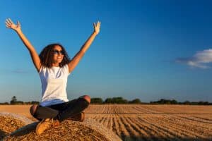 Image of a woman in a white shirt free from trauma symptoms sitting on a hay bale. You can find a 