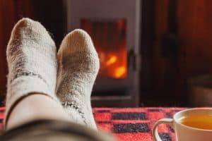 Image of a person in comfy socks propped up in front of a fire. Showing that you can start feeling healing in your comfy clothes with online therapy in North Carolina. With an online therapist you can have virtual therapy while in comfortable clothes in a place that is most beneficial for you.