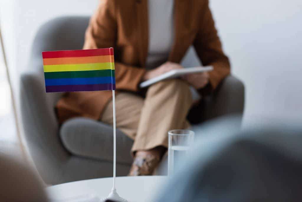 A close up of a pride flag on a desk of a person with a clipboard. This could represent the support an LGBTQ+ affirming therapist in North Carolina can offer.