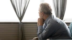 A man sits while looking out a window with a pensive look