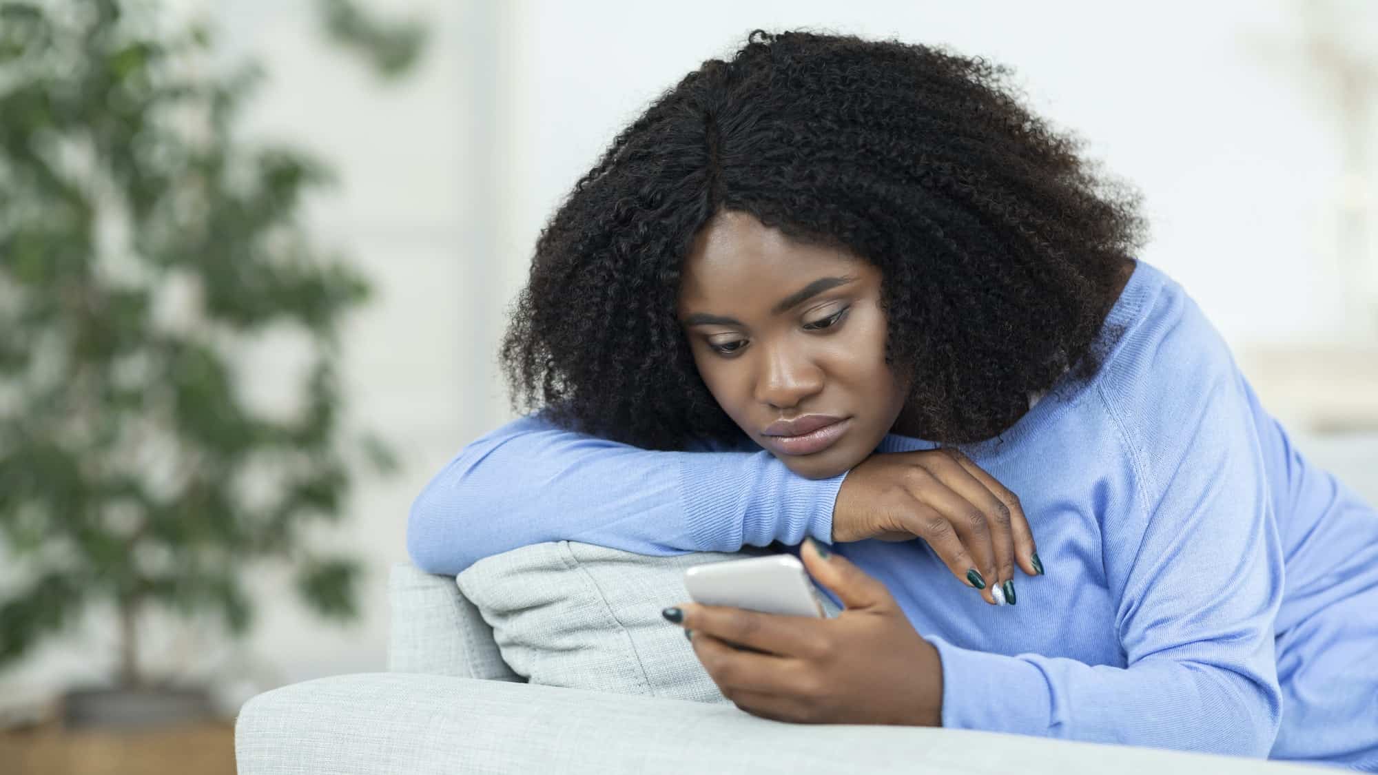 Frustrated lady checking mobile phone sitting on the couch